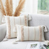 A beige and white striped boho tufted throw pillow cover with fringed tassels resting on a light gray sofa.