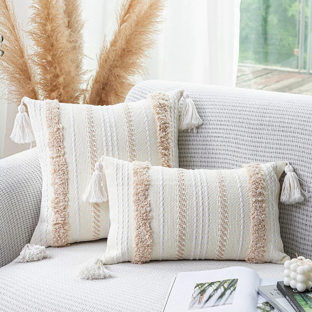 A beige and white striped boho tufted throw pillow cover with fringed tassels resting on a light gray sofa.