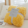 A yellow plush double-sided throw blanket with a textured jacquard pattern resting on a white cushion.