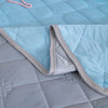 A light blue quilted blanket folded over a gray blanket, showing the soft texture and stitching.