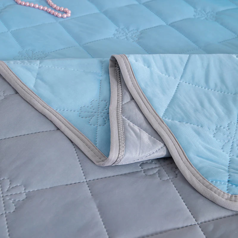 A light blue quilted blanket folded over a gray blanket, showing the soft texture and stitching.