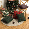 A set of two plaid decorative throw pillow covers in green and red tartan fabric displayed on a wooden chair and a rug.
