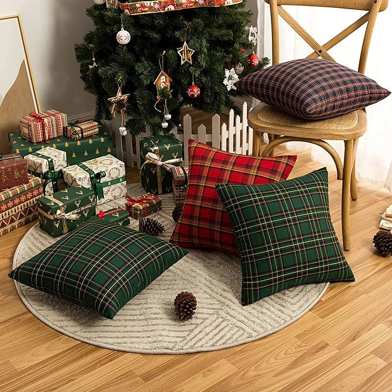 A set of two plaid decorative throw pillow covers in green and red tartan fabric displayed on a wooden chair and a rug.