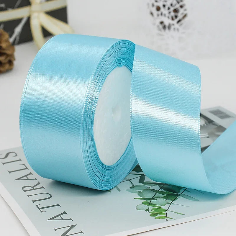 Roll of light blue satin craft ribbon with decorative trim shown on a white surface.