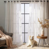 White sheer voile curtain panels hanging in a window frame with natural light filtering into a living room setting.