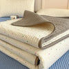 A stack of light beige quilted bedspreads with subtle floral patterns resting on a blue surface.