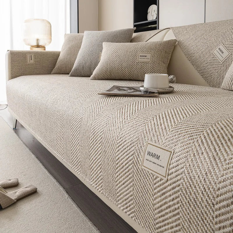 A beige linen sofa cover cushion with textured fabric and small labels is displayed on a bed.