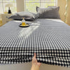 A black and white checkered flannel fitted sheet is displayed on a bed, with a hand touching the fabric.