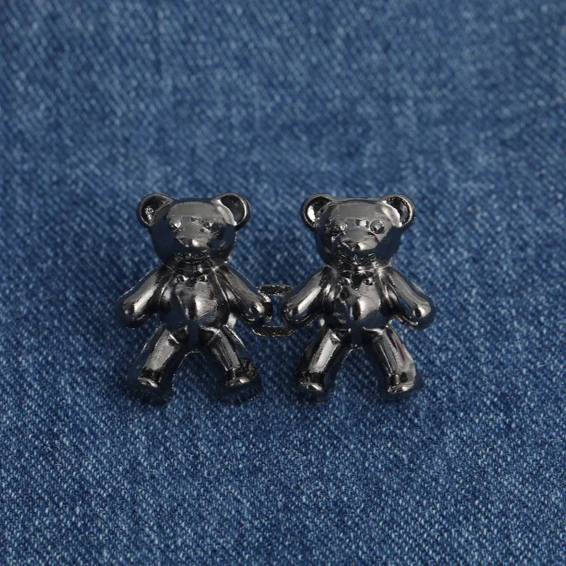 A pair of silver bear button pins are displayed on a blue denim fabric.