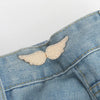 A small, delicate gold-toned feather button clip is pinned onto a blue denim jean fabric.