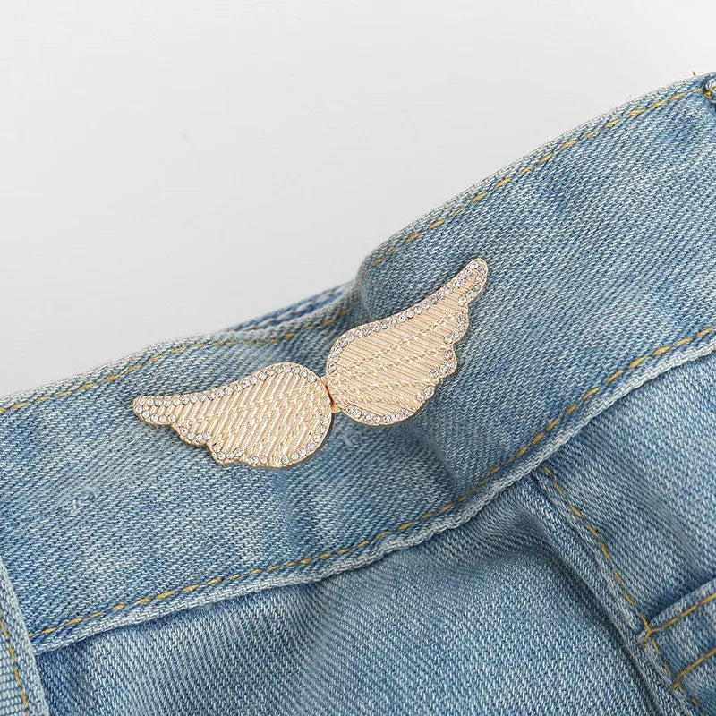 A small, delicate gold-toned feather button clip is pinned onto a blue denim jean fabric.