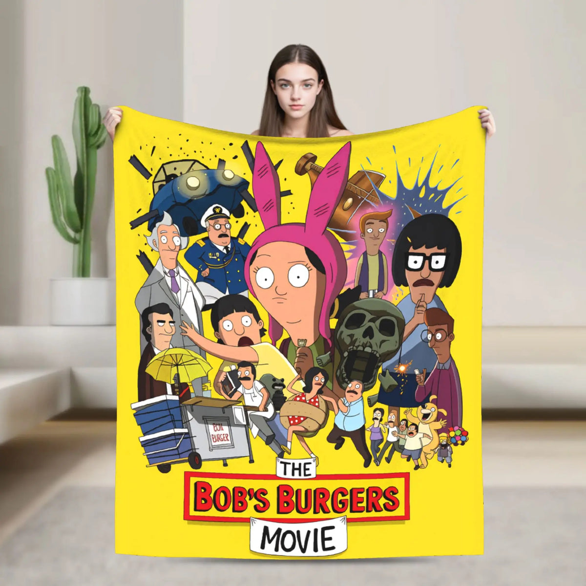 A yellow throw blanket featuring characters from The Bob's Burgers movie, including Tina Belcher and Gene Belcher.