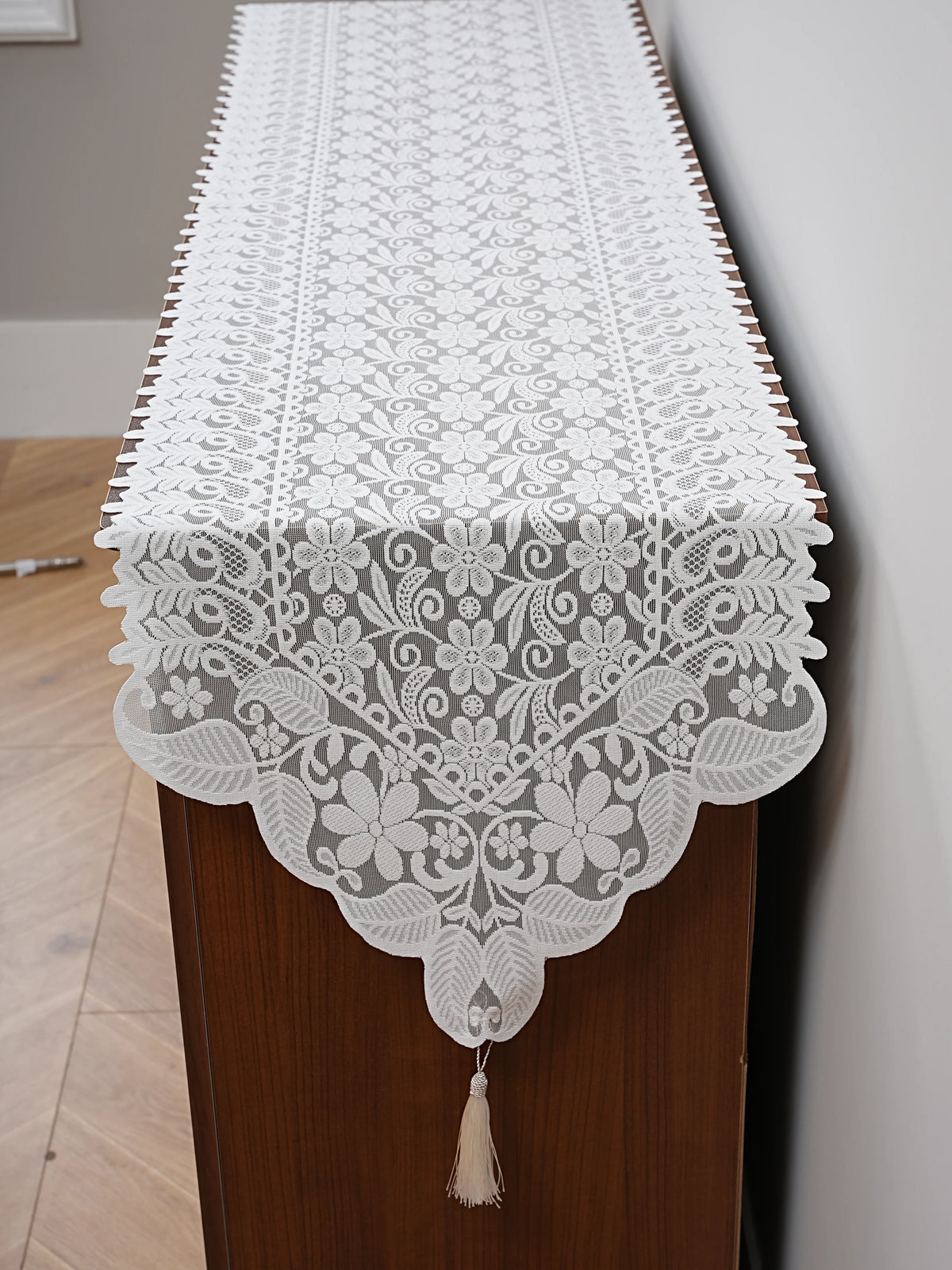White embroidered lace table runner displayed on a wooden cabinet.