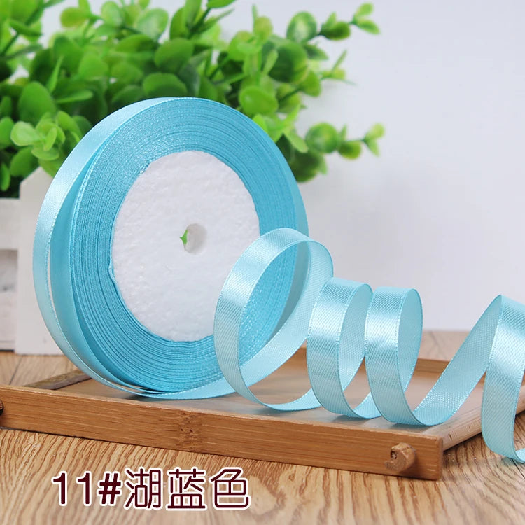 Roll of light blue satin ribbon with a white core displayed on a wooden board.