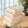 A stack of foldable bed sheet storage bags in various light pink and beige tones resting on a wooden table.