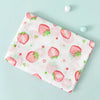 A pink muslin swaddle blanket featuring a pattern of red strawberries and green leaves on a light blue background.