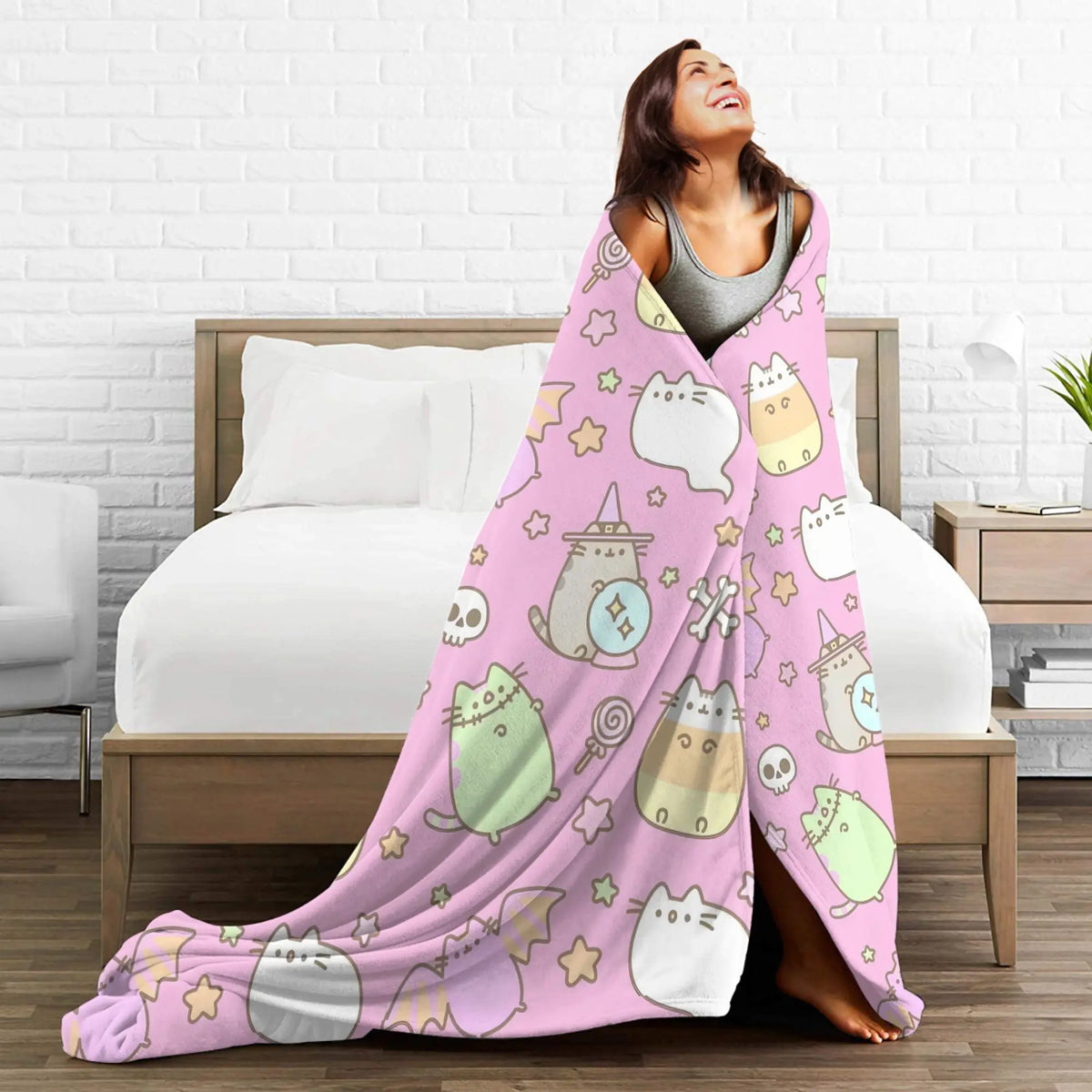 A woman is smiling while draped in a pink coral fleece throw blanket featuring cute cat designs on a white background.