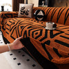 A hand touches an orange and black patterned knit sofa protector with a decorative pillow and a teacup on the fabric.