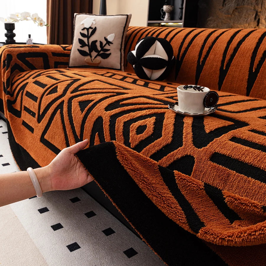 A hand touches an orange and black patterned knit sofa protector with a decorative pillow and a teacup on the fabric.