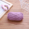 A ball of purple flat thread yarn lying on a wooden surface next to a framed drawing and a white wire mesh basket.