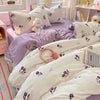A white and purple duvet cover set with matching pillowcases and a small stuffed animal on a bed.