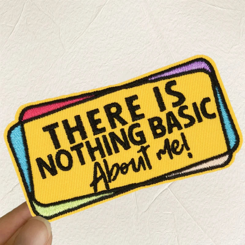 A yellow embroidered patch with black text that reads THERE IS NOTHING BASIC ABOUT ME