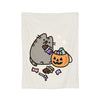 A cute gray cat plush toy is shown with a carved pumpkin and scattered treats on a white blanket.