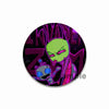 An enamel pin featuring a stylized green alien character with purple accents against a dark background.