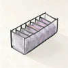 A black foldable drawer organizer rack holding folded pink and white undergarments.