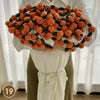 A hand knitted floral rose bouquet throw blanket featuring orange and green roses displayed on a white fabric.