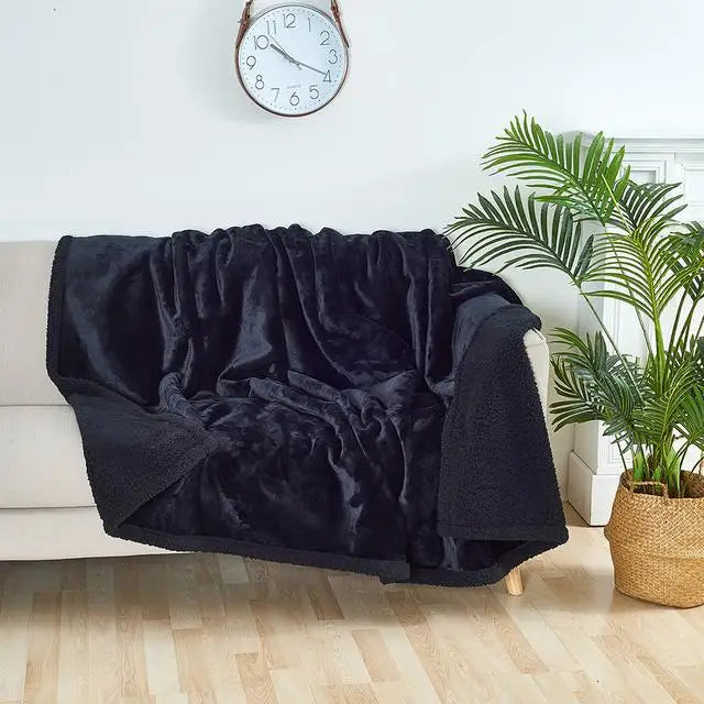 A black shaggy blanket draped over a white sofa next to a potted green plant.