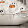 A white knitted throw pillow cover decorated with orange pumpkin and ghost patterns.