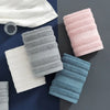A set of four textured face towels in shades of white, light pink, gray, and blue are displayed on a dark surface.