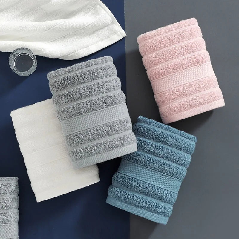 A set of four textured face towels in shades of white, light pink, gray, and blue are displayed on a dark surface.