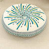 A round cushion with a bohemian pattern featuring radiating lines in teal, yellow, and black on a light background.
