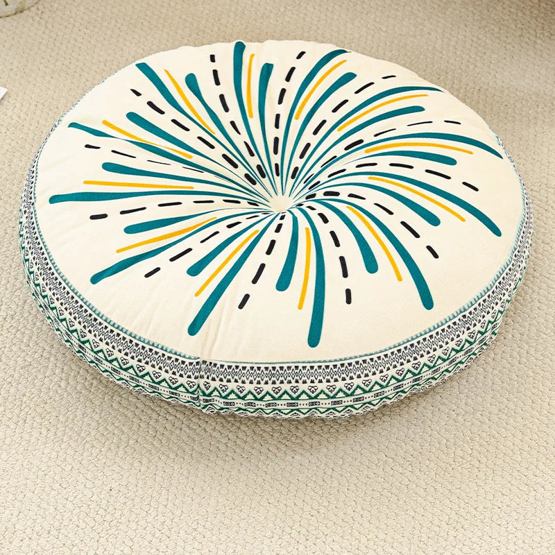 A round cushion with a bohemian pattern featuring radiating lines in teal, yellow, and black on a light background.