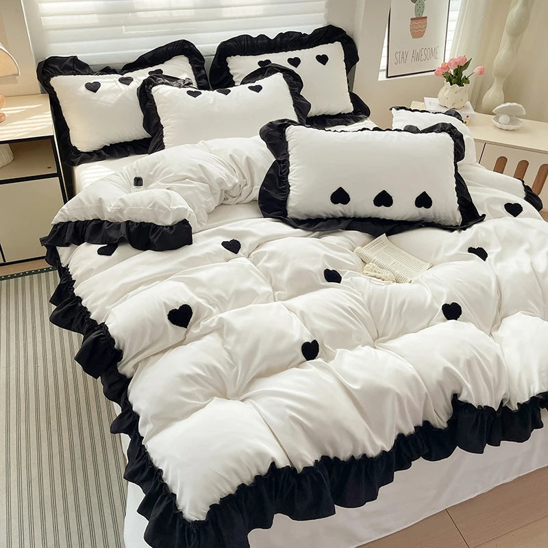 A white duvet set with black embroidered hearts and black trim, featuring decorative pillows.