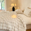 A white faux fur throw blanket is draped over a bed, next to a black lamp and pillows.