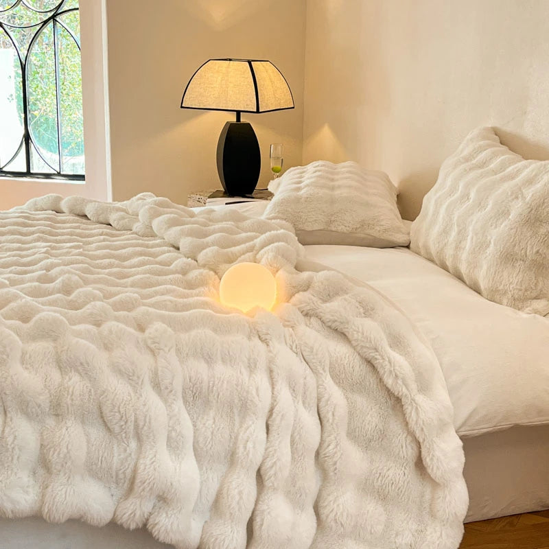 A white faux fur throw blanket is draped over a bed, next to a black lamp and pillows.