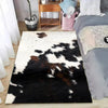 A black and white faux cowhide pattern area rug placed on a wooden floor next to a bed.