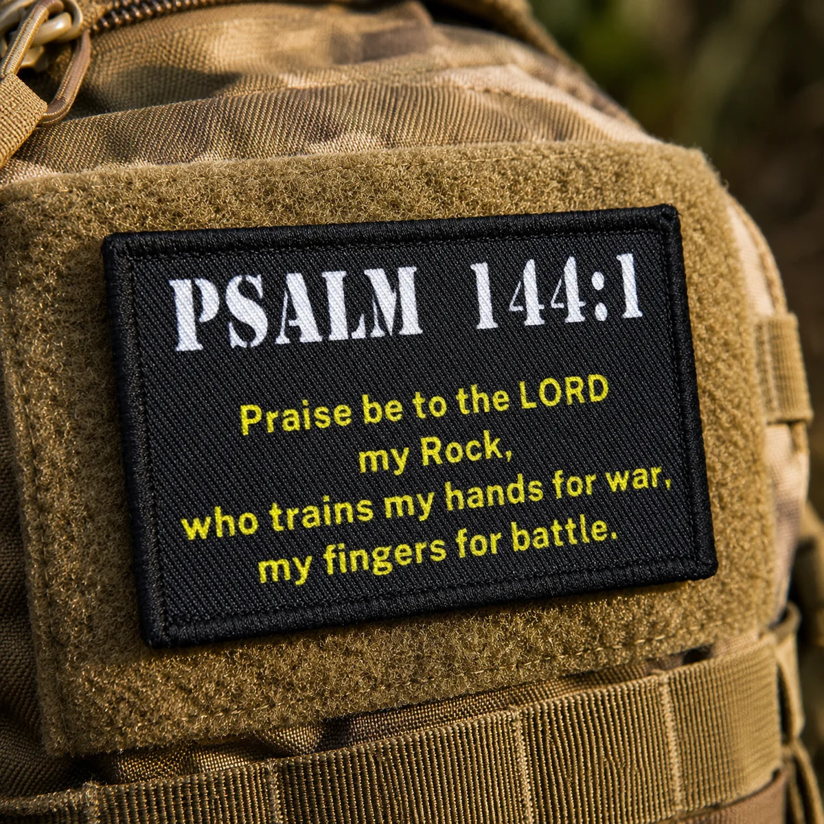 A close-up of a tan military vest featuring a black embroidered patch with the text Psalm 144:1.