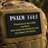 A close-up of a tan military vest featuring a black embroidered combat patch with the text Psalm 144:1.