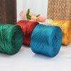 A collection of metallic cake colored yarn spools in green, red, blue, and gold resting on a white surface.