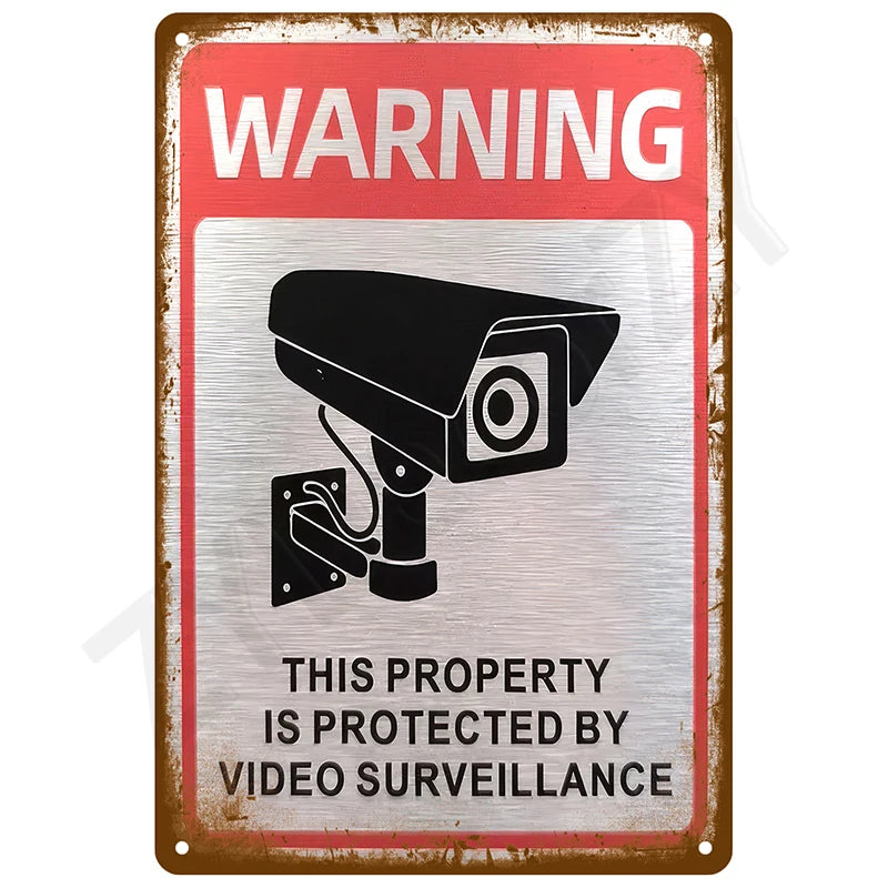 A vintage metal warning sign with a red background and silver border featuring an icon of a security camera.