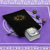 A black velvet pouch with a gold sun design holds a stack of tarot cards on a purple patterned surface.