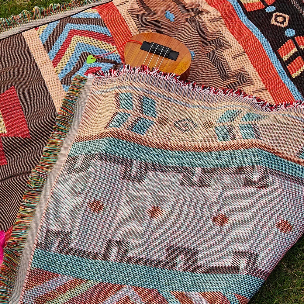 A woven blanket featuring geometric patterns in shades of orange, blue, and beige laid out on grass with a wooden instrument 