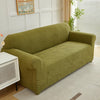 A olive green sofa slipcover featuring a jacquard leaves pattern in a light olive tone, placed in a bright room.