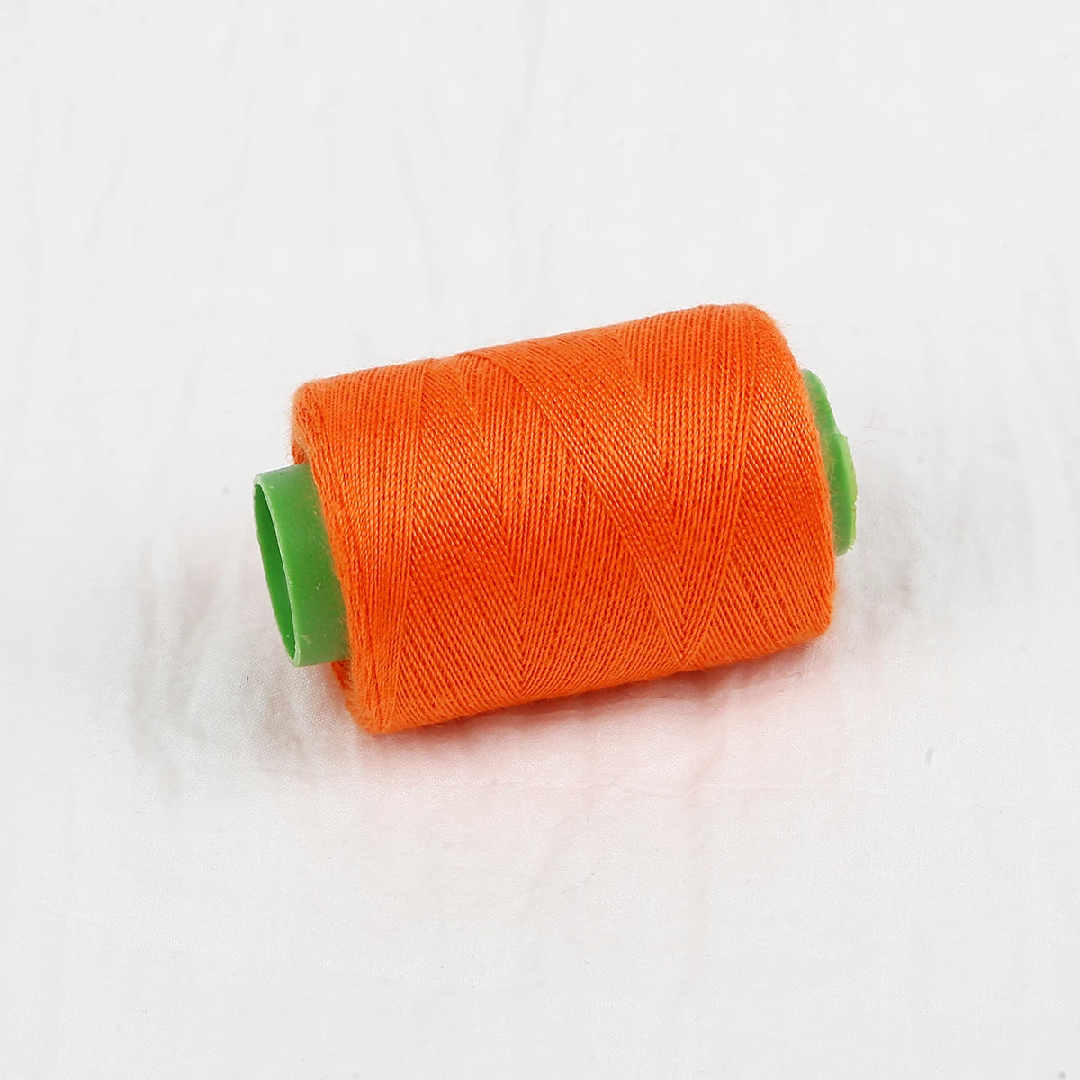A spool of bright orange handmade sewing thread with a green core.
