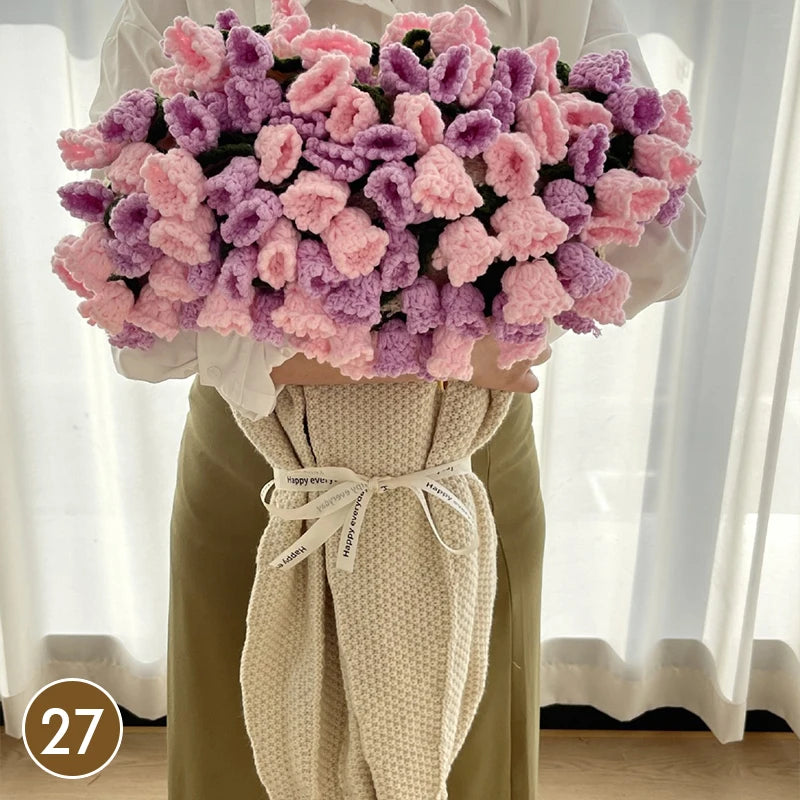 A hand knitted floral rose bouquet throw blanket in shades of pink and purple displayed against a white background.