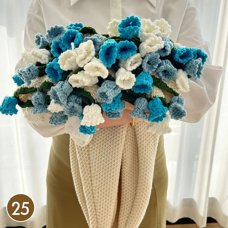 A hand knitted floral rose bouquet featuring blue and white flowers displayed against a white shirt and beige fabric.